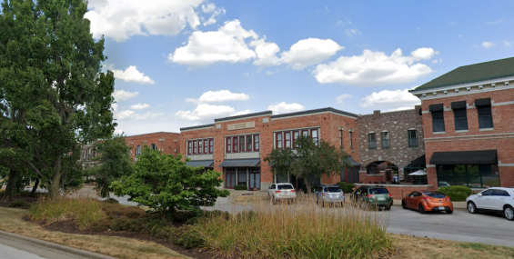 A wider view of Chesterfield Mixed-Use, showing its red brick exterior and surrounding greenery. The building is set back from the street with a landscaped area in the foreground. The neighboring structures share a similar architectural style, creating a cohesive, upscale commercial setting.