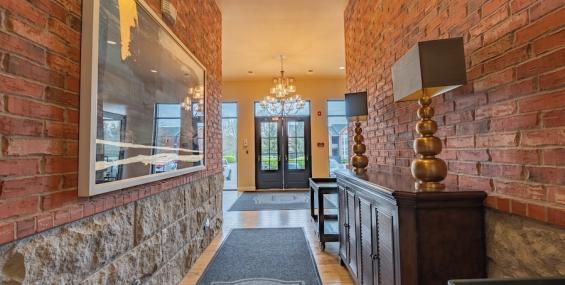 he interior of Chesterfield Lofts II, showcasing a stylish lobby with exposed red brick walls and stone accents. A long hallway leads to the glass entrance doors, illuminated by elegant chandeliers. Decorative gold lamps sit atop a wooden console table, adding a touch of sophistication to the space.