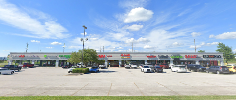 A wide-angle view of Nixa Center, a retail shopping plaza in Nixa, MO, featuring a single-story strip mall with multiple storefronts. Visible businesses include Murney Associates, H&R Block, Pet Supplies Plus, Cato, El Lago Mexican Restaurant, Top Nails, Halo Hair Studio, Springfield Vapors, Sally Beauty, and Sun Tan City. The parking lot in front of the center has numerous cars parked, with a few trees and light poles scattered throughout. The sky is bright blue with scattered clouds, creating a clean and 